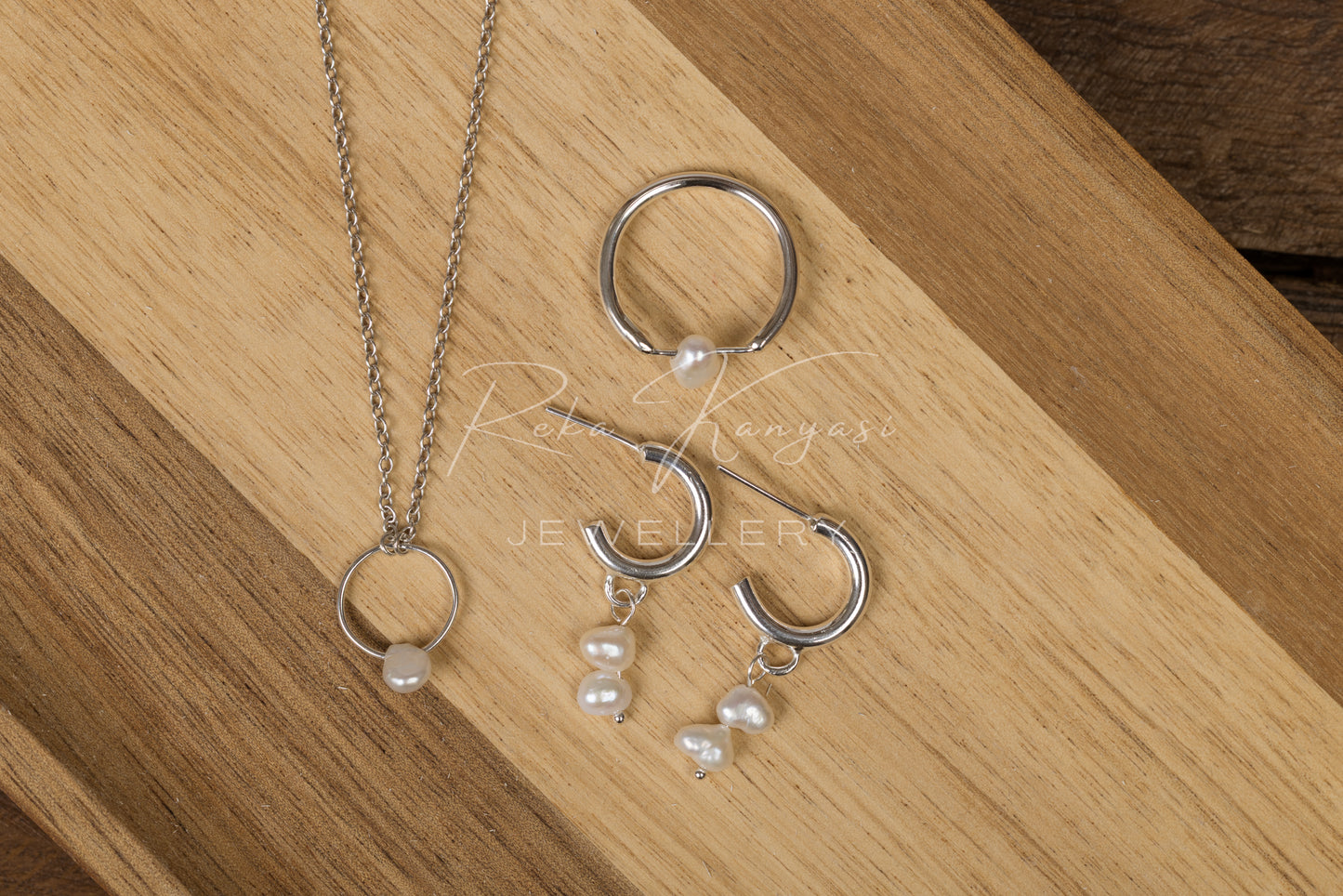 Silver jewelry set with rings and pearl accents on a wooden surface
